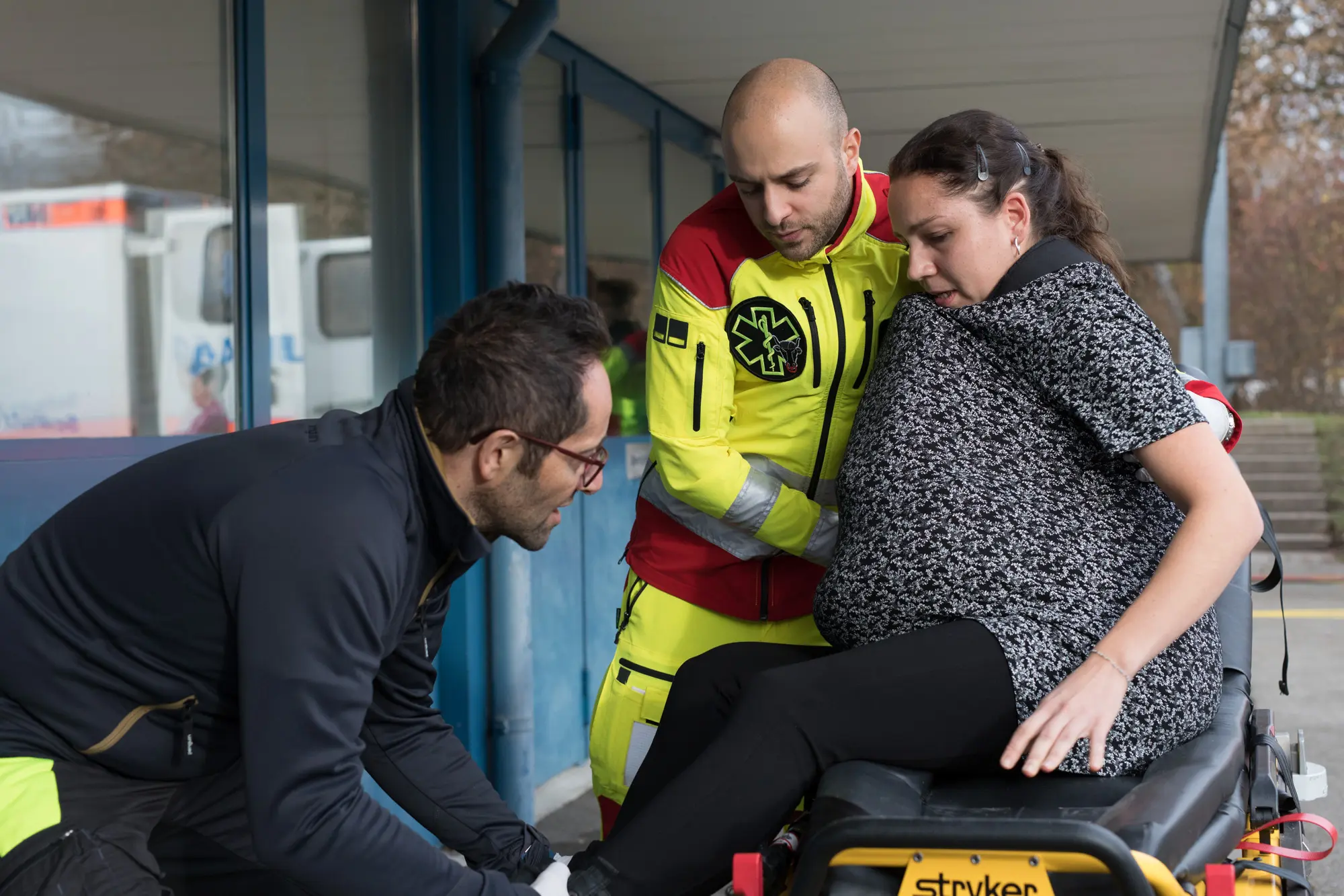 Eine Hebammenstudentin spielt eine Gebärende, sie muss sich auf die Bahre legen, die Sanitäter sprechen ihr gut zu.