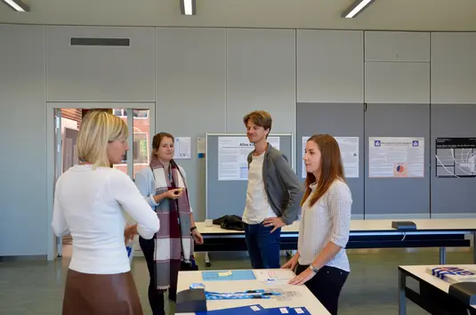 Konferenzbüro. Zwei Teilnehmende unterhalten sich mit zwei Personen des Konferenzteams.