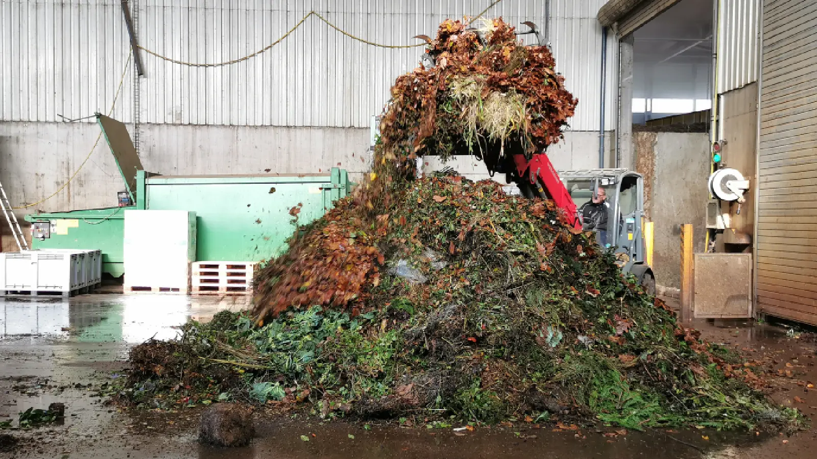 Grüngutabfall wird in einer Halle mit einem Bagger gemischt