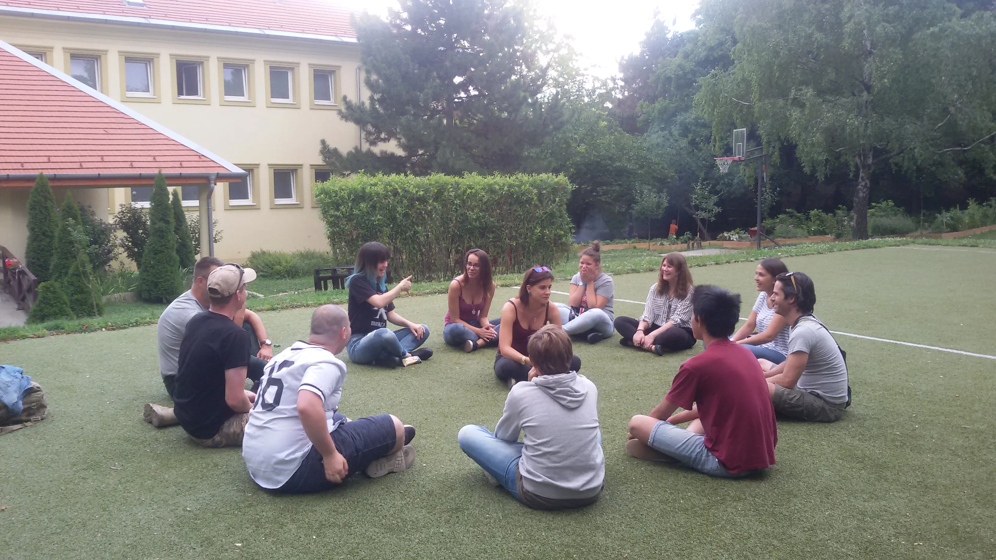 Junge Leute sitzen im Kreis im Gras vor einem Heim und diskutieren angeregt.