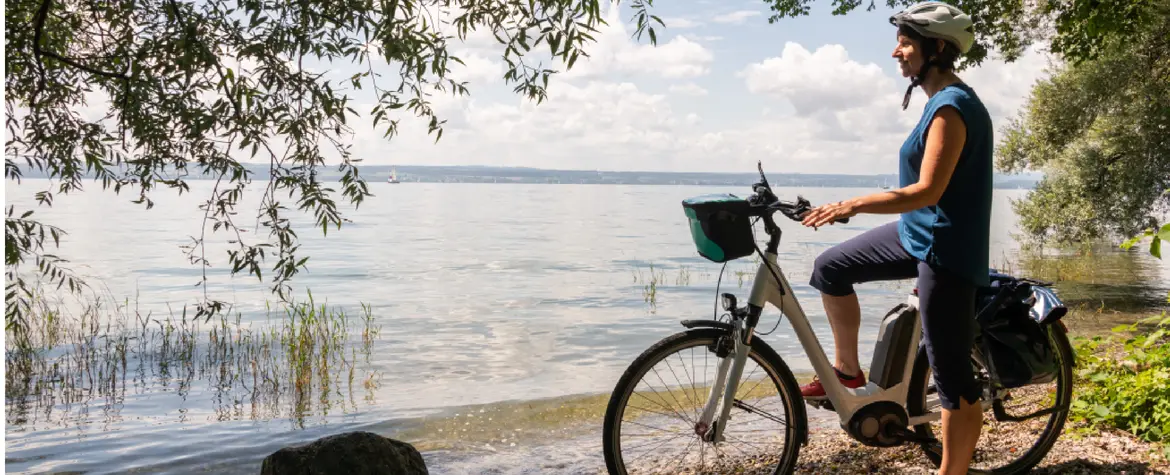 A woman stands by her bike on the lakeshore and looks out over the lake.