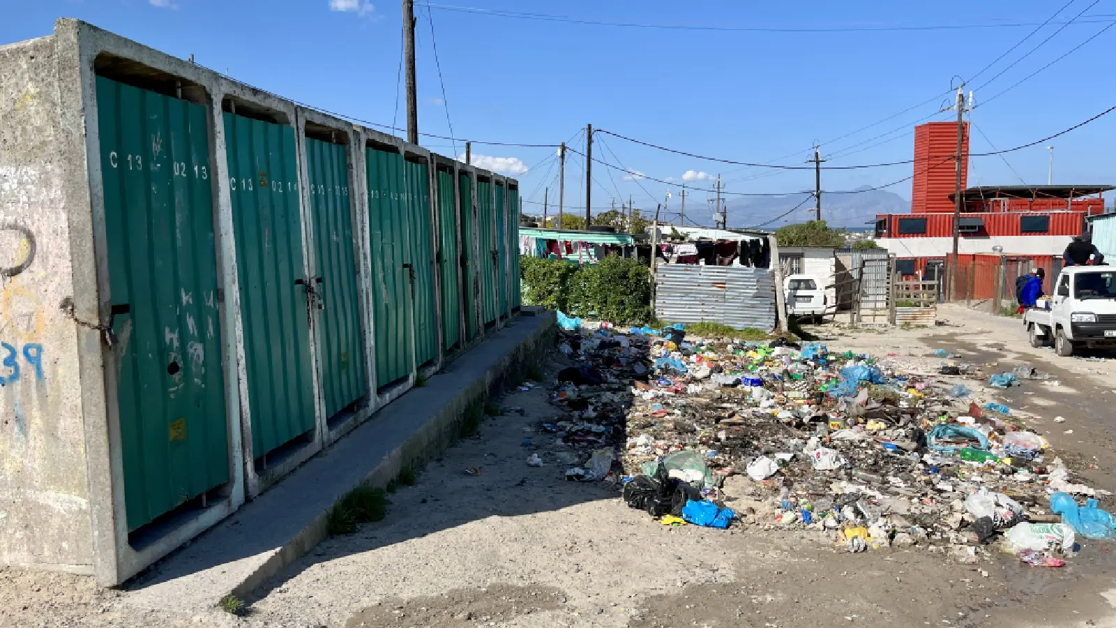 Approximately ten public toilets in the informal settlement, located side by side in a concrete building and separated from each other. The toilet doors are green.