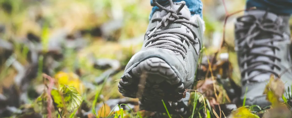 Ausschnitt der Füsse einer Person, die mit Wanderschuhen durch eine Wiese geht.